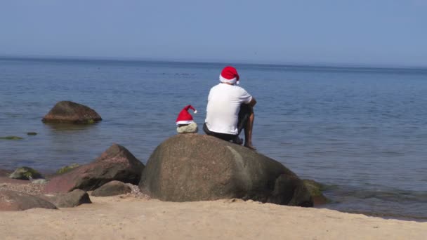 Hombre Sienta Roca Paseo Marítimo Con Sombrero Santa Claus — Vídeo de stock