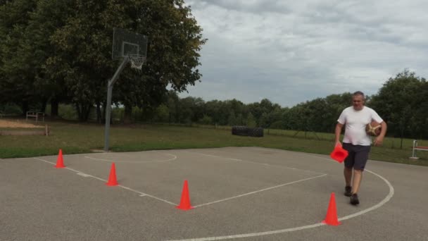 Sportler Sammelt Orangenkegel Vom Basketballplatz Ein — Stockvideo