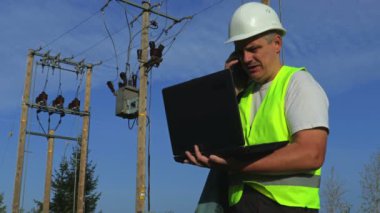 Elektrikçi akıllı telefonda konuşurken taşınabilir bilgisayarla