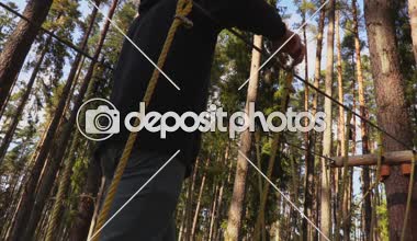 Kamera ağaçlar arasında kablolar üzerinde yürüyen adam takip eder.