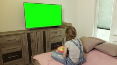 Küçük kız cips yiyor ve yeşil ekran ile Tv izliyor