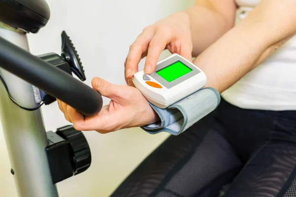 Woman on exercise bike after workout checking blood pressure on green screen