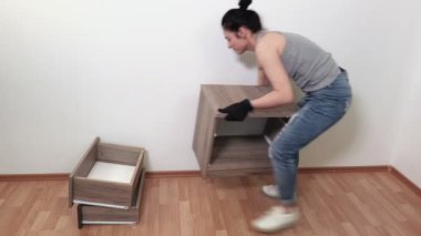 Kadın boş odada komidinin yerini değiştiriyor.