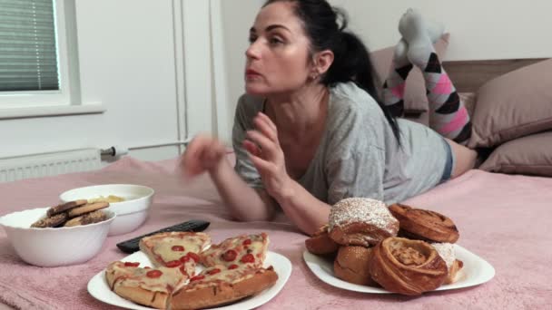 ベッドに横たわり 甘いパンとピザを食べている女性 — ストック動画