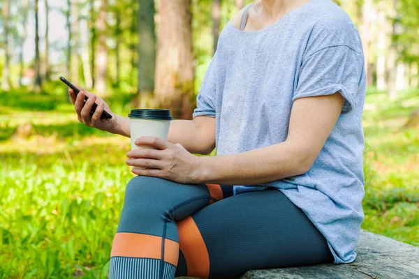 公園のベンチでコーヒーとスマートフォンを持ち去る女性 — ストック写真