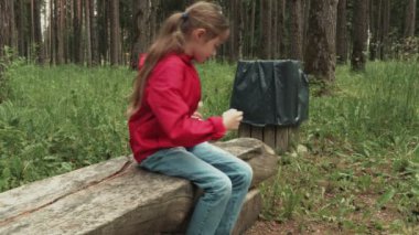 Çöp konteynerinin yakınındaki parkta bankta alkolsüz içecek olan küçük kız