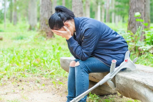 公園でベンチで泣いて松葉杖を持つ負傷女性 — ストック写真