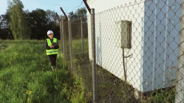 フェンスの近くに女性エンジニアの書き込みと歩く — ストック動画