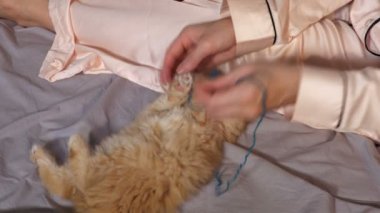 Kadın yatakta oturuyor ve kedi yavrusuna yardım ediyor.