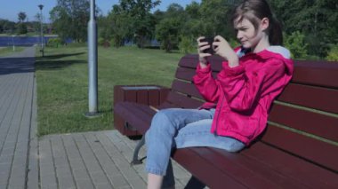 Akıllı telefon kullanan ve bankta oturan kız.