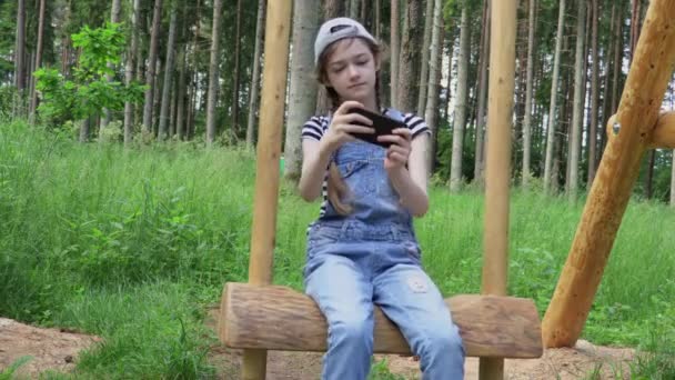 Kleines Mädchen Genießt Schaukel Und Spielt Spiel Auf Smartphone — Stockvideo