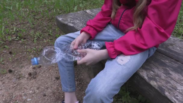 小さな女の子オンベンチ絞る空のプラスチックボトル — ストック動画