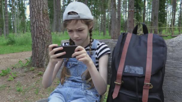 Κοριτσάκι Σακίδιο Και Smartphone Στον Πάγκο Στο Πάρκο — Αρχείο Βίντεο