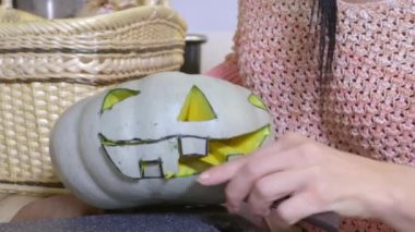 Bıçaklı bir kadın Cadılar Bayramı için balkabağının üstünde yüzünü hazırlıyor.