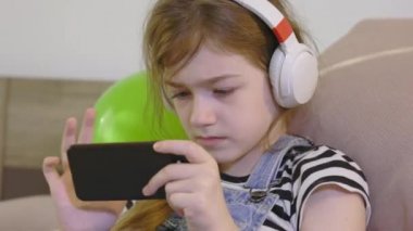 Kulaklıklı akıllı küçük kız cep telefonu kullanıyor.