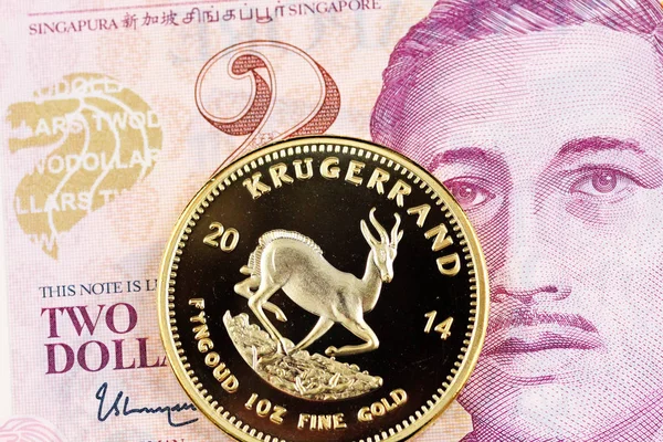 A two Singapore dollar bill with a golden one ounce Krugerrand coin