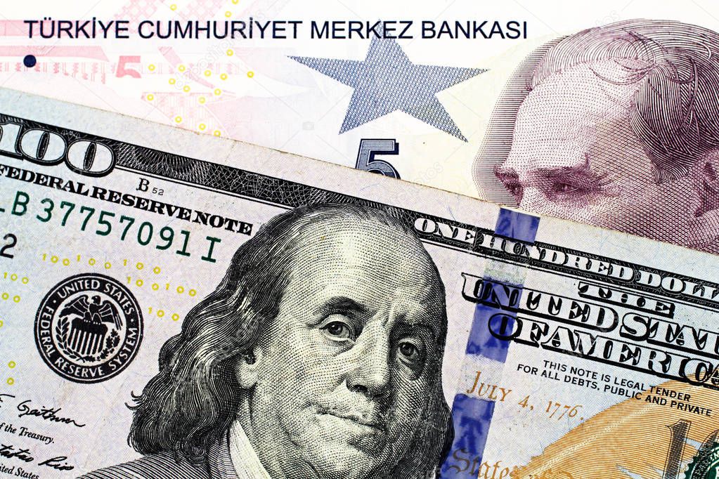 A close up image of a blue American one hundred dollar bill with a five Turkish lira bill