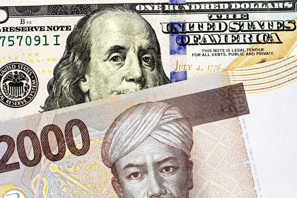 A blue American one hundred dollar bill with a two thousand Indonesian rupiah bank note close up