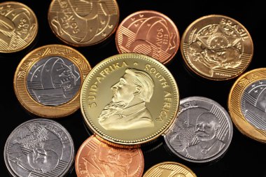 A macro image of miscellaneous Brazilian coins with a South African one ounce gold Krugerrand coin on a black reflective background close up  clipart