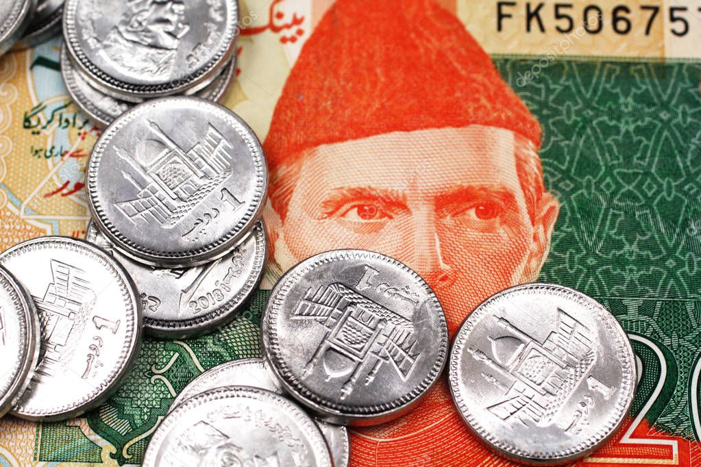 A close up image of a pile of one rupee coins from Pakistan on a twenty Pakistani rupee bank note