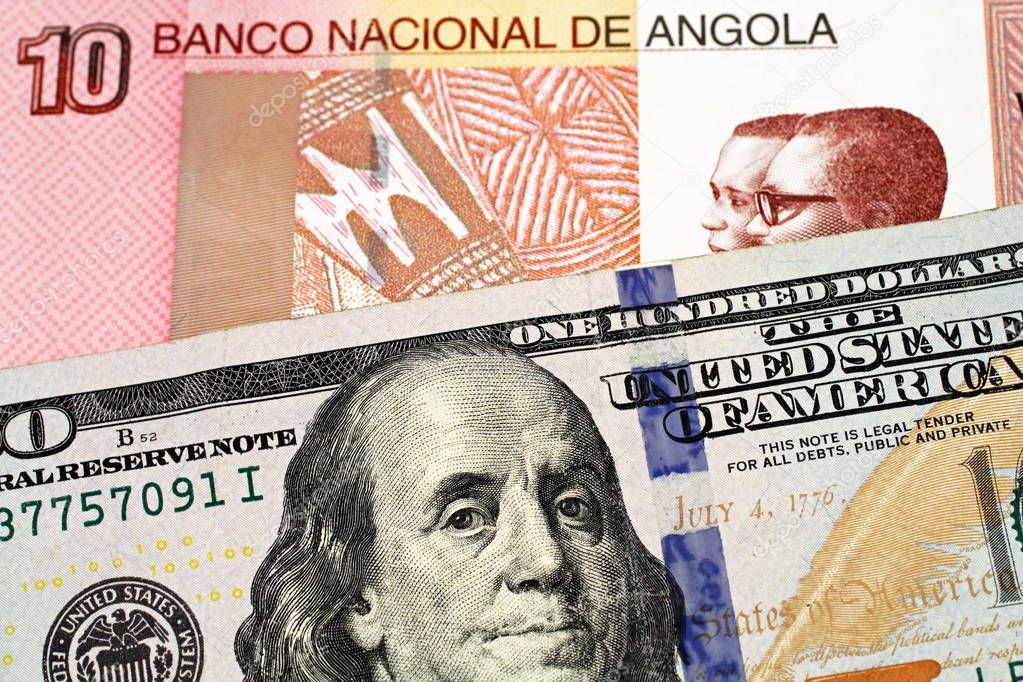 A macro image of a colorful Angolan ten kwanza bill with an American one hundred dollar bill close up