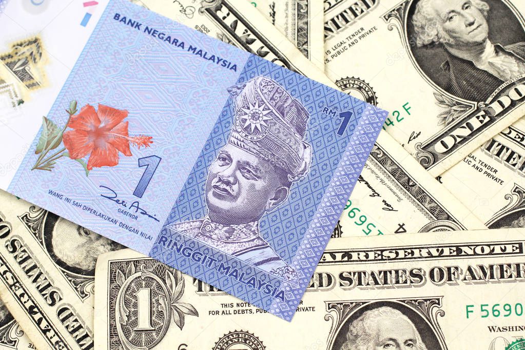 A close up image of a blue one Malaysian ringgit bank note on a bed of American one dollar bills close up in macro