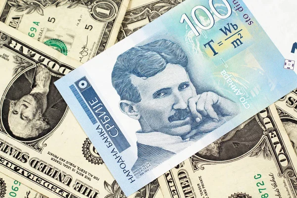 A close up of a blue and white, one hundred Serbian dinar bank note on a background of American one dollar bills