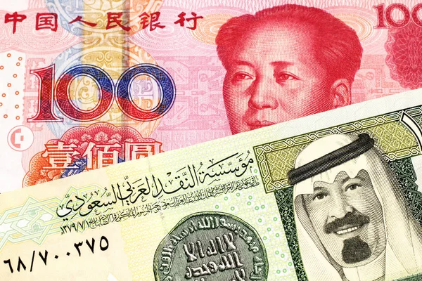 A green one riyal bank note from Saudi Arabia with a red, Chinese one hundred yuan bank note close up in macro