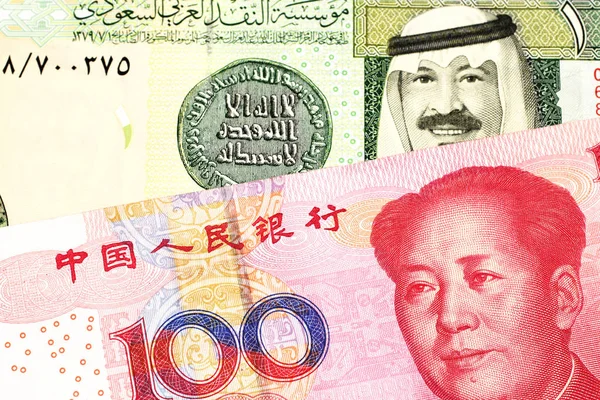 A green one riyal bank note from Saudi Arabia with a red, Chinese one hundred yuan bank note close up in macro