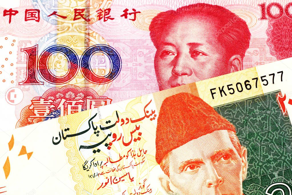 An orange and green twenty Pakistani rupee bank note with a red one hundred Chinese yuan bank note in macro