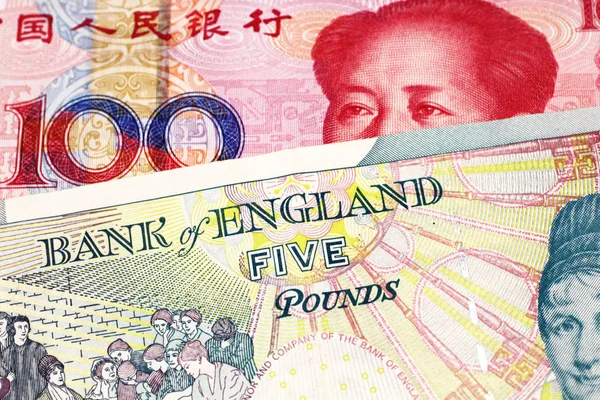 A five pound British pound sterling with a red, one hundred yuan Chinese renminbi bank note close up in macro
