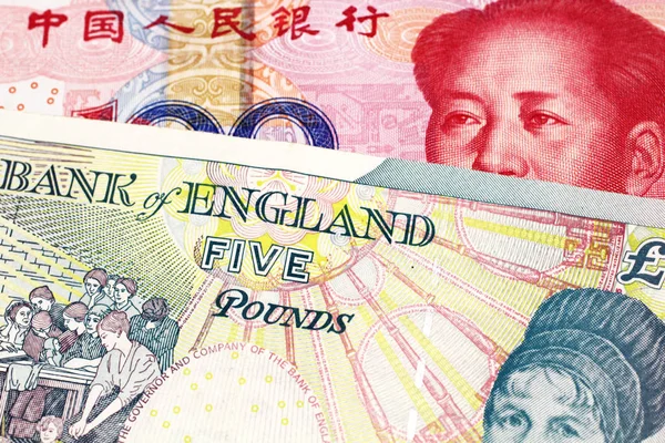 A five pound British pound sterling with a red, one hundred yuan Chinese renminbi bank note close up in macro