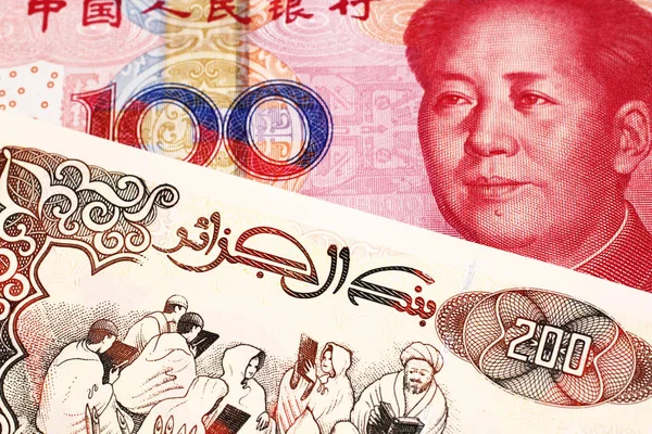 A beige, two hundred Algerian dinar bill with a red, Chinese renminbi one hundred yuan bank note close up in macro