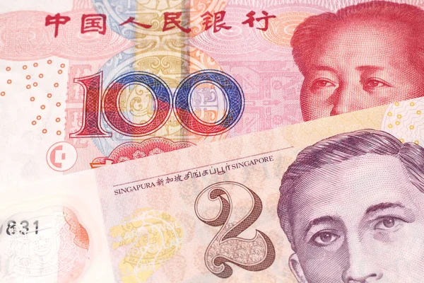 A close up image of a red, one hundred yuan bank note from the People\'s republic of China, in macro with a two dollar bill from Singapore