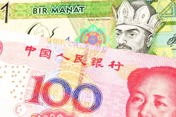 A green one manat note from Turkmenistan close up in macro with a red, one hundred yuan renminbi bank note from the People\'s Republic of China