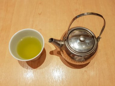 Çelik çaydanlık ve beyaz ahşap desen masa üstü arka plan, Tayland bardakta sıcak Japon yeşil çay içme