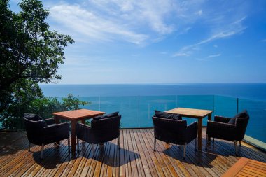 Tablolar ve rattan açık koltuk ahşap güverte ve cam balkon panoramik Andaman okyanus deniz görünümü, yeşil ağaç ve mavi gökyüzü arka plan, Phuket, Tayland ile ayarlama
