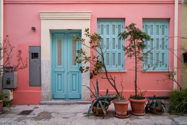 Güzel kentsel sahne cephe arka planda pastel pembe bina boya duvar sıva, ışık mavi giriş kapısı ve windows ile yeşil bitki kapları, Atina, Yunanistan