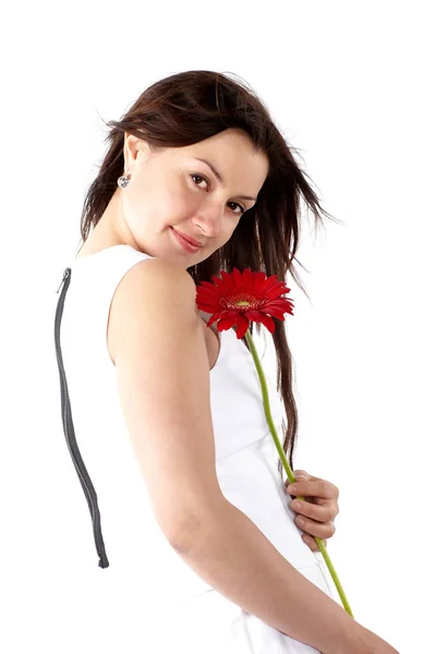 Schöne junge Frau in weißem Kleid, posiert seitlich mit roter Blume und blickt in die Kamera — Stockfoto