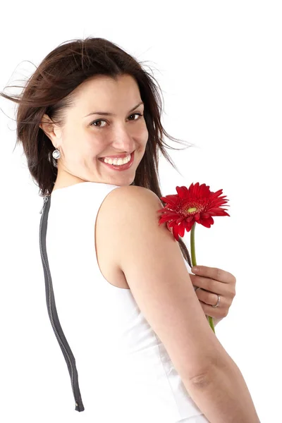 Schöne junge Frau in weißem Kleid, posiert seitlich mit roter Blume, blickt in die Kamera und lächelt — Stockfoto