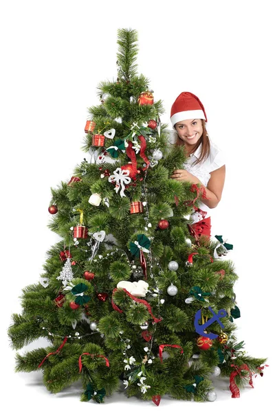 Schöne lächelnde Frau mit Weihnachtsmütze, hinter dem Weihnachtsbaum, isoliert auf weiß — Stockfoto