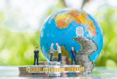 Minyatür işadamı el sıkışma küre ve taahhüt, anlaşma, yatırım ve ortaklık iş kavramı arka plan coins kullanarak büyüyen yığınları ile topluca spinner üzerinde.