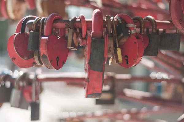 Muchas cerraduras de metal envejecidas rojas en forma de corazón en el rodillo en un día soleado, primer plano, luz suave, fondo borroso . — Foto de Stock