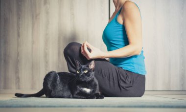 Evde yoga yapan bir kadın. Yanında oturan siyah kedi.