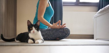 Evde yoga yapan bir kadın. Yanında oturan siyah kedi.
