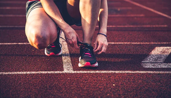 koşu pistinde genç kadın ayakkabılarını bağlayarak