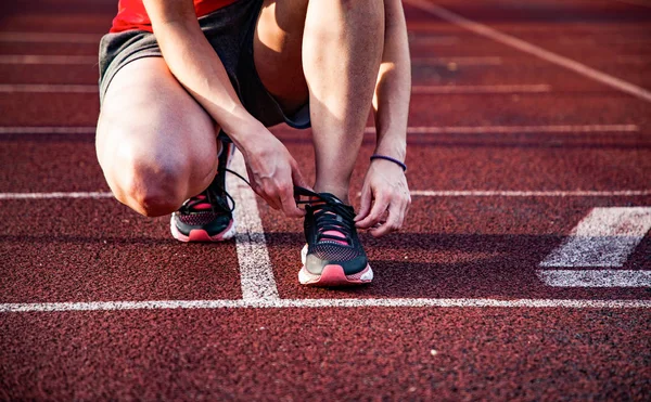 Young woman on running track lacing her shoes — Stock Photo, Image