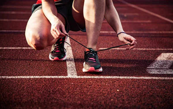 Young woman on running track lacing her shoes — Stock Photo, Image