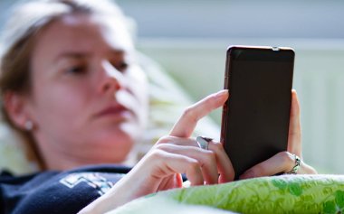 Kadın yatakta yatarken akıllı telefon kullanıyor.