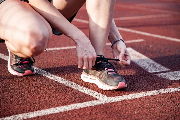 Koşu pistinde genç kadın ayakkabılarını bağlayarak — Stok fotoğraf